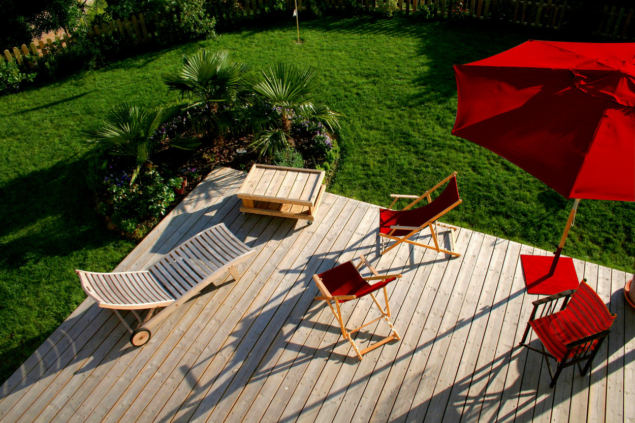 terrasse aus Holz, auf dem zwei Hängestühle und eine Liege aus Holz stehen sowie ein roter Sonnenschirm. terrasse aus Holz, auf dem zwei Hängestühle und eine Liege aus Holz stehen sowie ein roter Sonnenschirm.